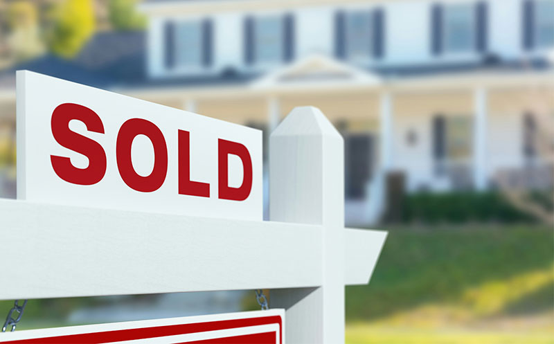 A red and white Sold sign in front of a blurred suburban home, representing a successfully sold property in the Twin Cities real estate market